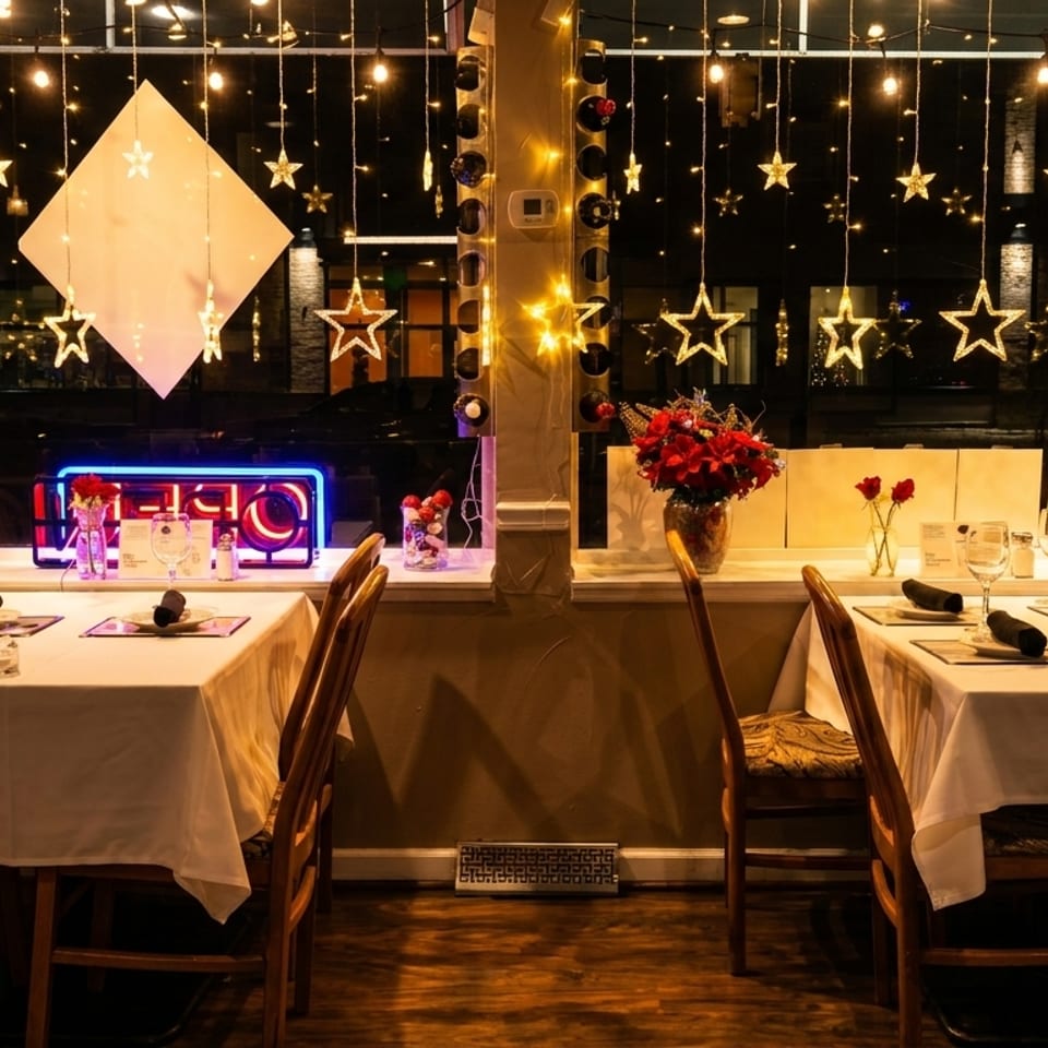 Restaurant dining room with two tables set for dinner, illuminated by star-shaped string lights in the window.