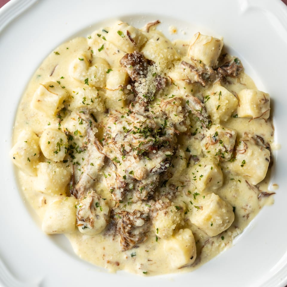 Creamy gnocchi topped with mushrooms, grated cheese, and chopped parsley on a white plate.
