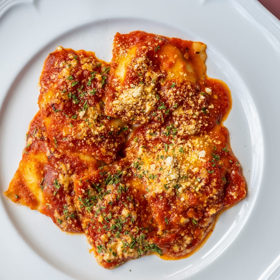 Ravioli topped with tomato sauce, grated cheese, and parsley on a white plate.