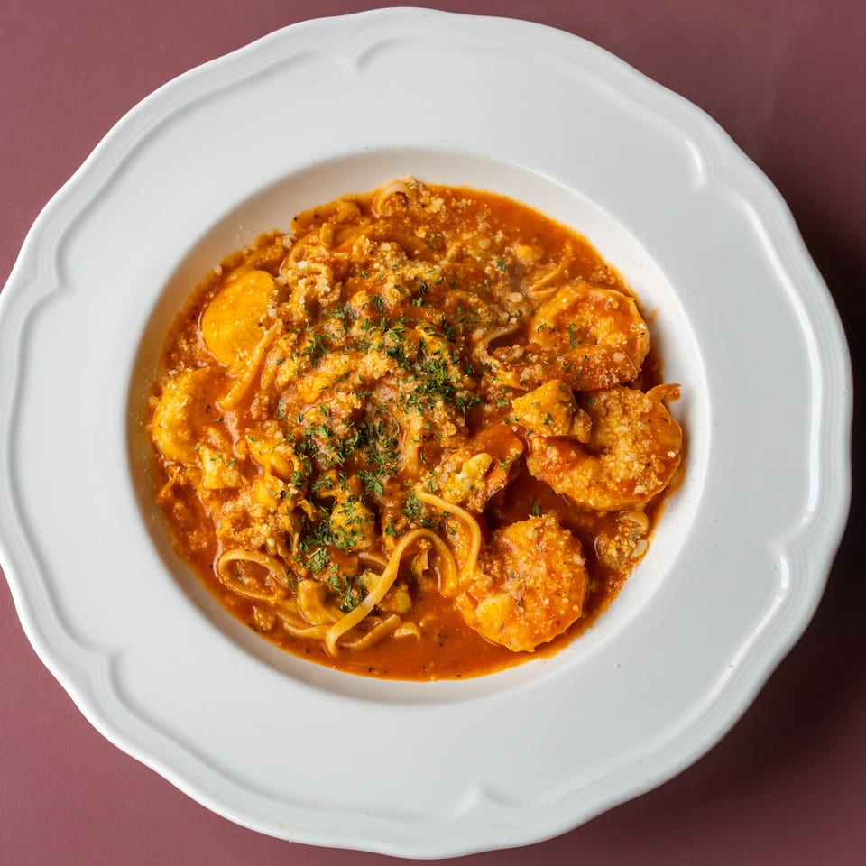 Pasta with shrimp in rich tomato sauce, topped with grated cheese and herbs, served on a white plate.