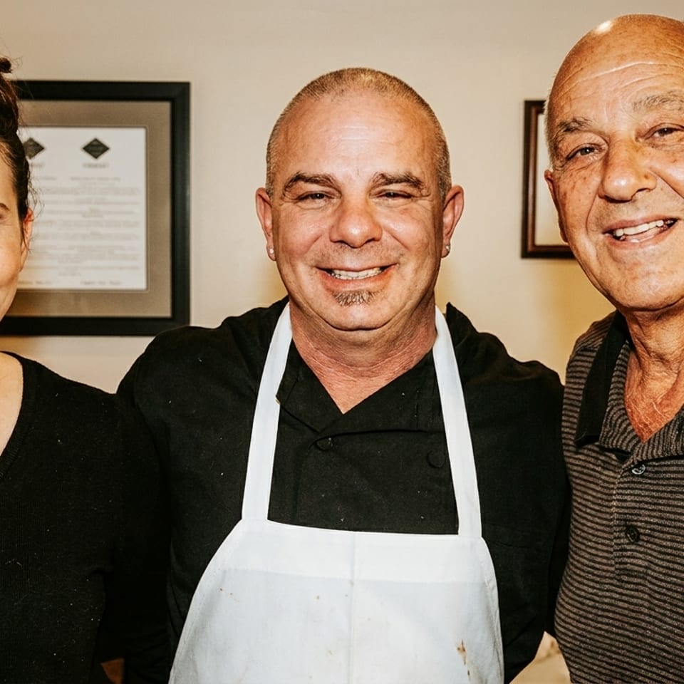 Three smiling restaurant staff members, two men and one woman, stand together indoors.