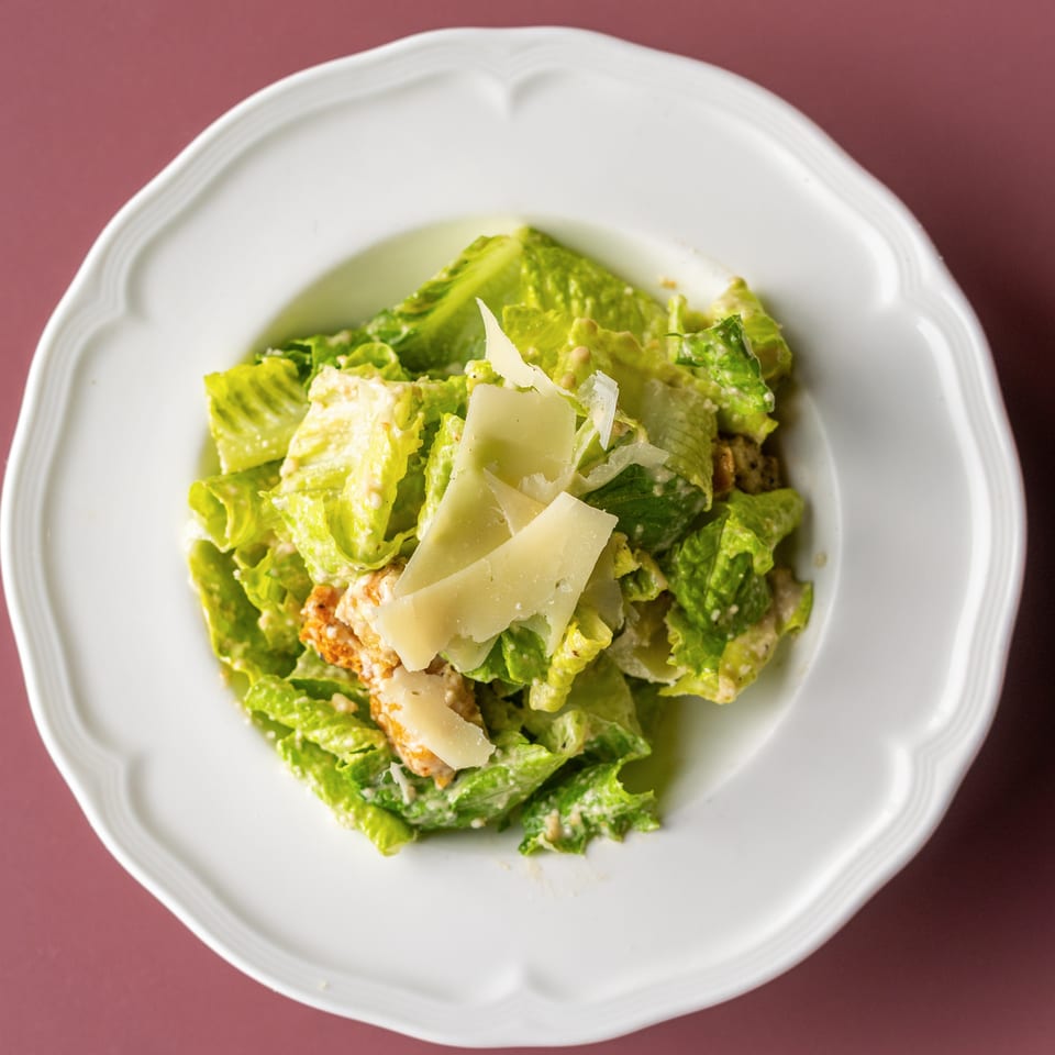 Caesar salad with romaine lettuce, creamy dressing, grilled chicken, and shaved Parmesan in a white bowl.