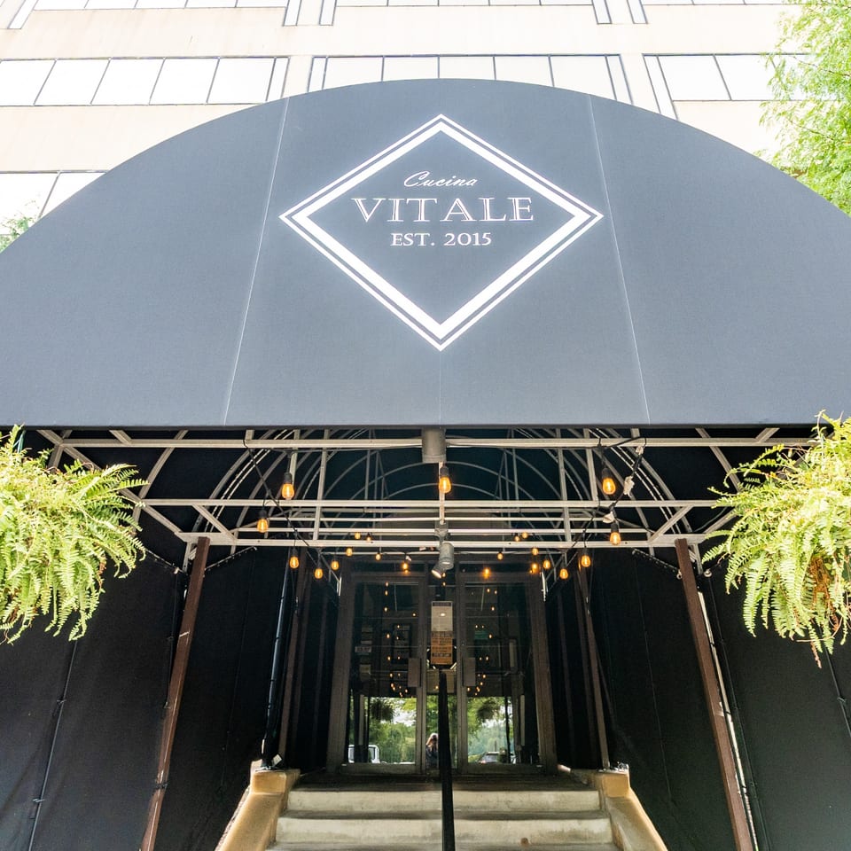Cucina Vitale entrance beneath its branded awning with hanging ferns.