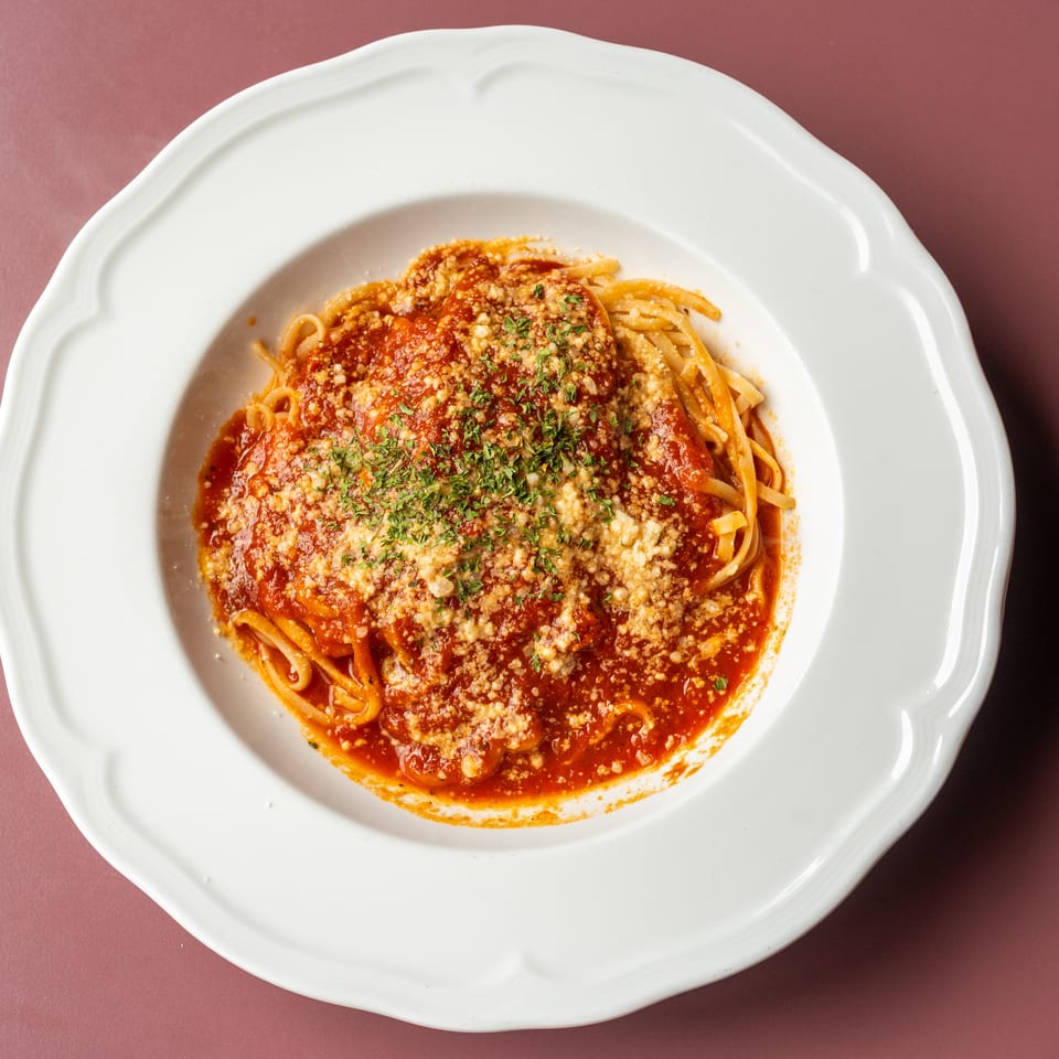 Spaghetti topped with red tomato sauce, grated cheese, and chopped herbs in a white scalloped bowl.