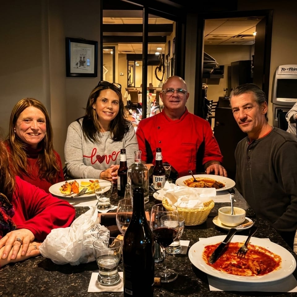 Six smiling people enjoy dinner and drinks at a restaurant table with plates of food.