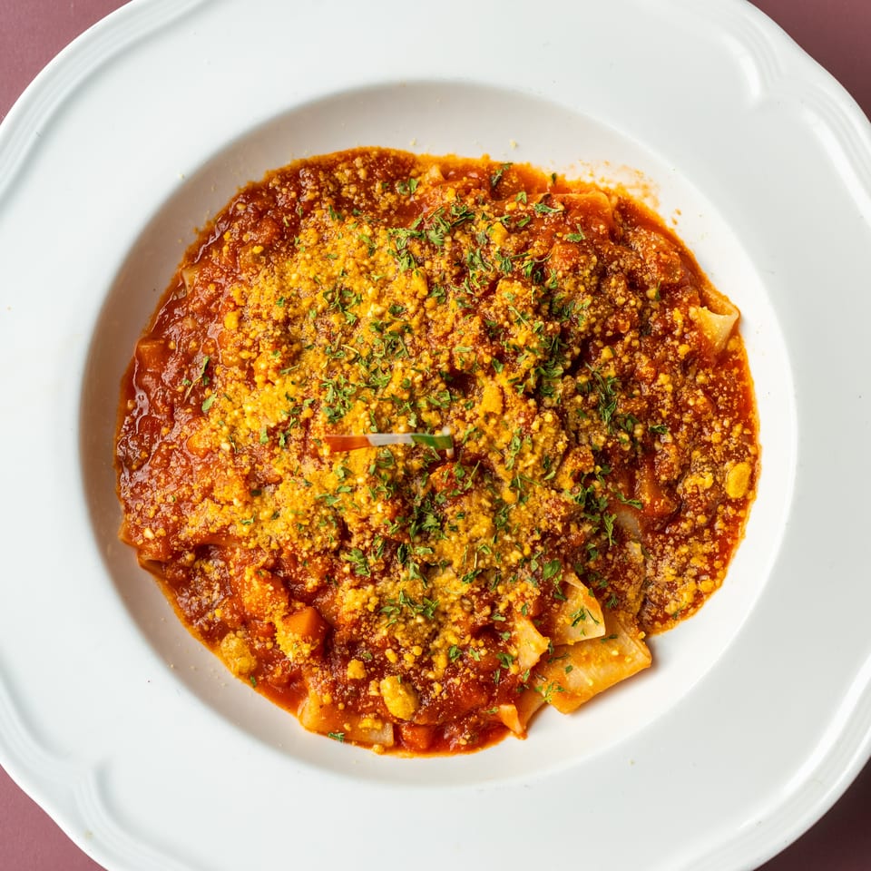 Ravioli covered in red tomato sauce, crumbled cheese, and chopped herbs on a white plate.