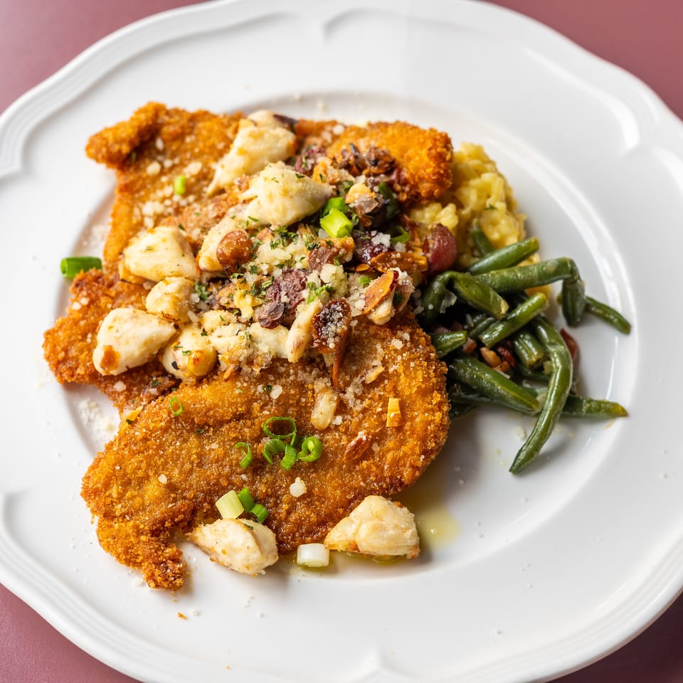Crispy breaded cutlets topped with chicken, mushrooms, herbs, and nuts, served with green beans and mashed potatoes.