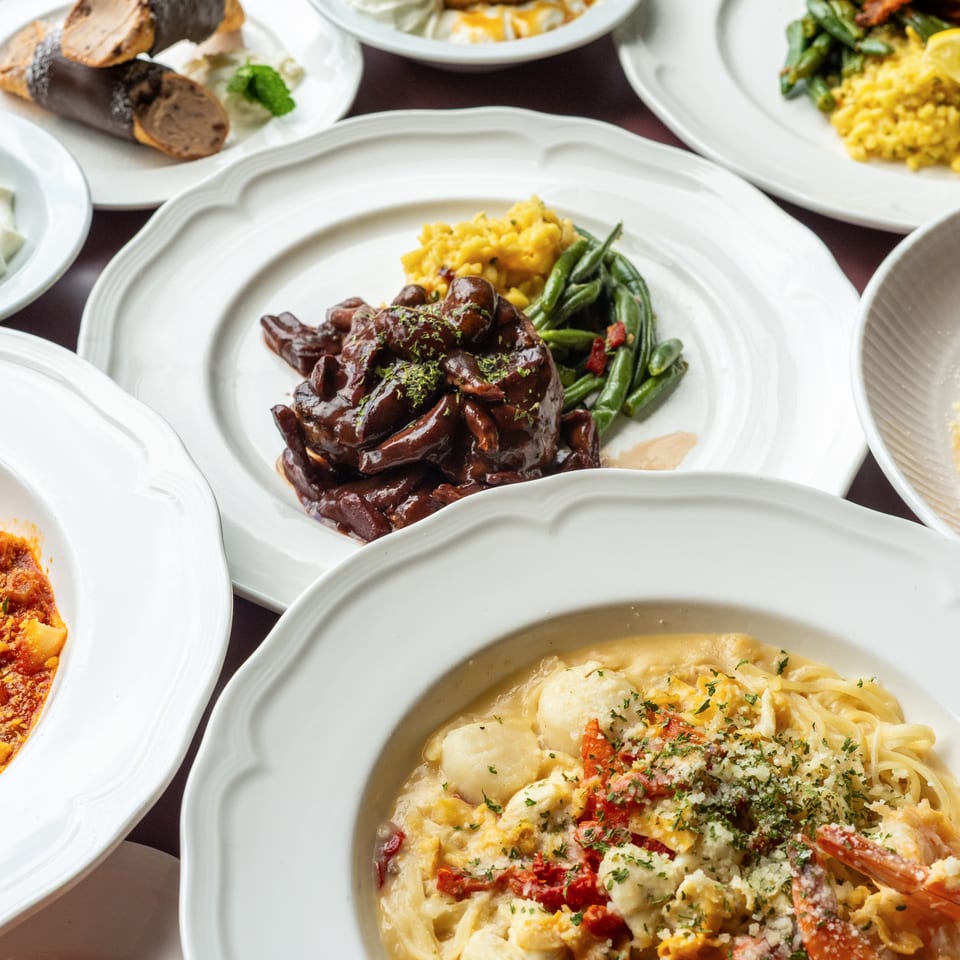 Assortment of plated dishes, including glazed meat, vegetables, pasta, seafood, and colorful sides, arranged on white restaurant plates.